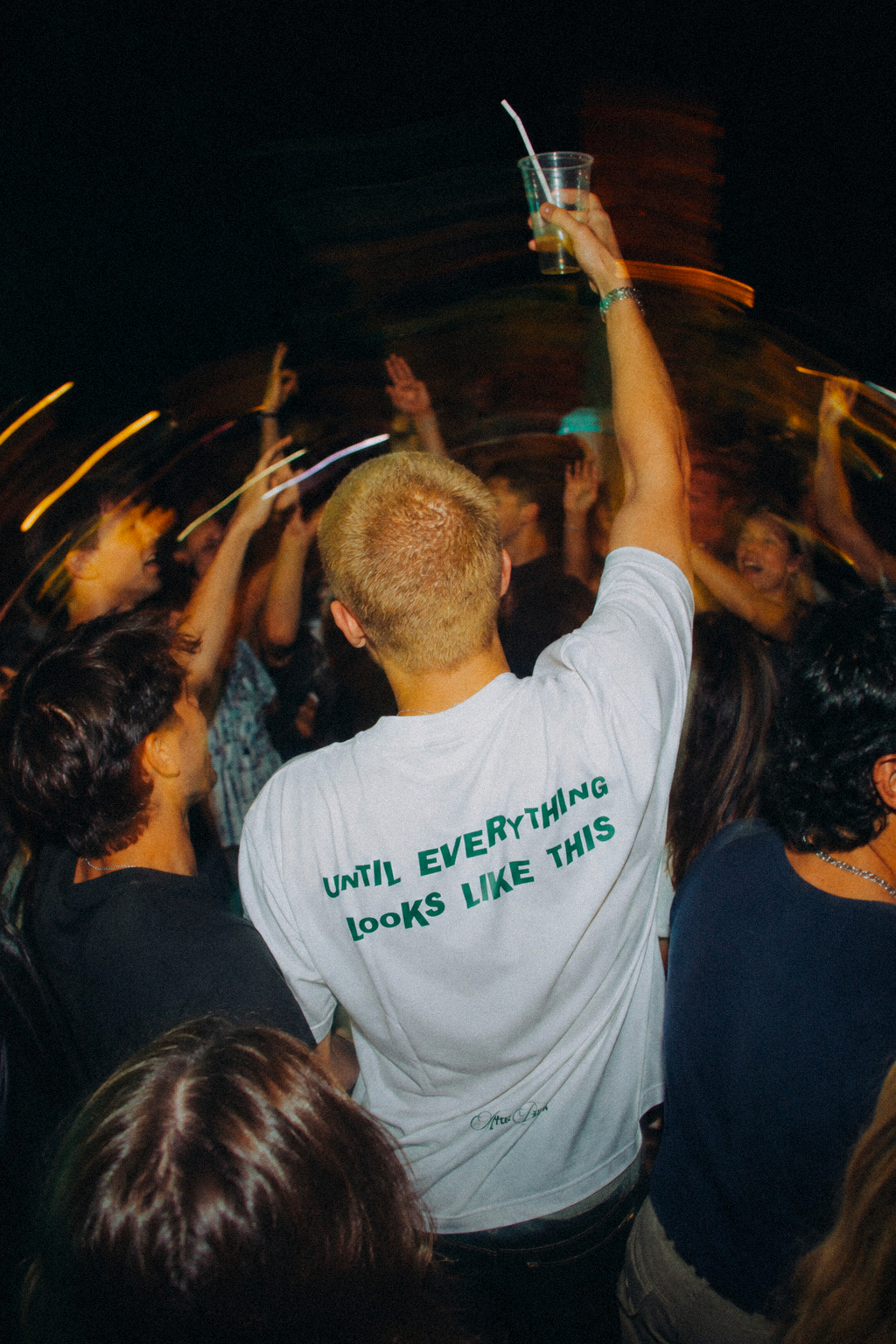 Modello indossa la t-shirt oversize bianca UNTIL EVERYTHING LOOKS LIKE THIS di 4AM Season con grafica verde sul retro durante una serata
